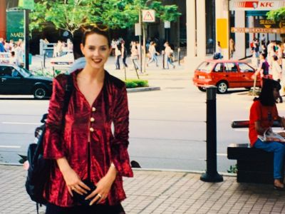 Suanne Braun is on a red dress and carrying a bag as she is posing for the picture.